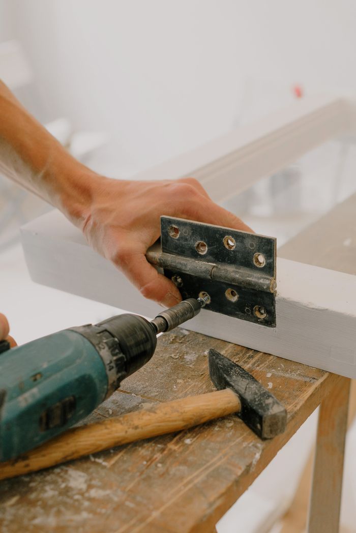 Crop d’un artisan méconnaissable fixant une charnière métallique avec un tournevis moderne sur un cadre de fenêtre en bois posé sur une planche de bois pendant des travaux de rénovation