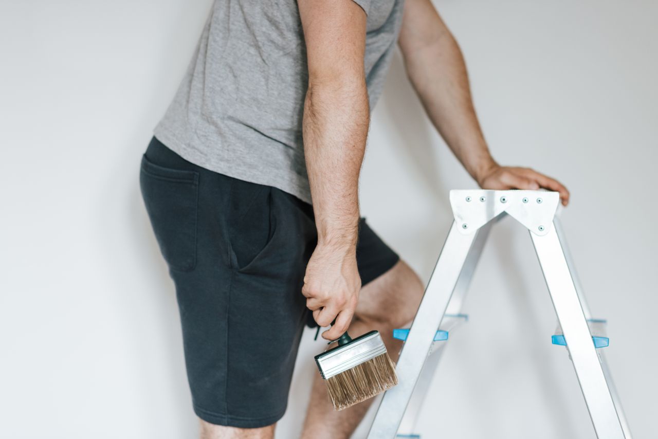 hero-img Side view of crop anonymous male decorator in casual clothes preparing to painting walls of light room while standing on stepladder